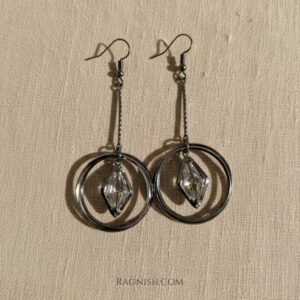 RAGNISH Ethereal Orbit Earrings. Gunmetal drop earrings with double hoop and suspended rhombus-cut clear crystal on beige fabric.