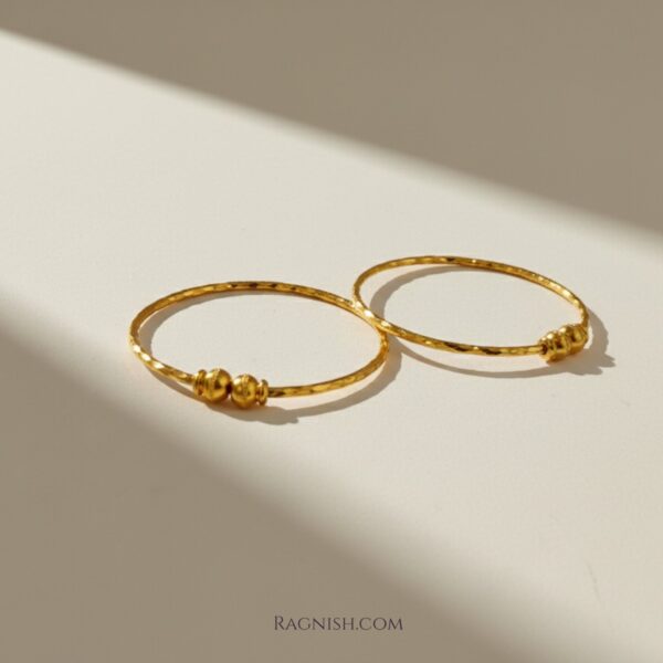 Close-up of two hammered gold-finish bangles with polished accent beads.