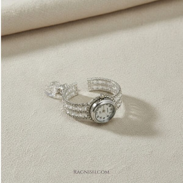 Luxury crystal-embellished cuff bracelet watch in silver tone on a neutral beige background.