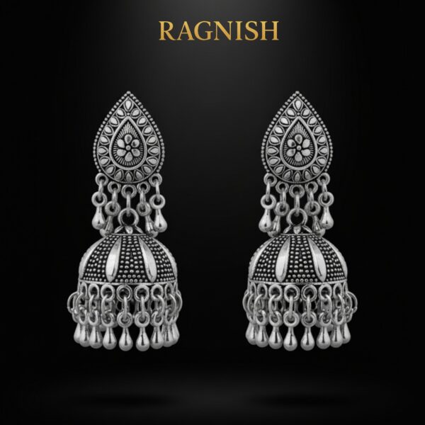 Close-up of oxidized metal jhumka earrings by RAGNISH, highlighting the detailed floral pattern and dangling silver bead charms.