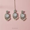 Close-up of Mirror Glaze Kundan chandelier earrings with pearl drops on textured beige background.