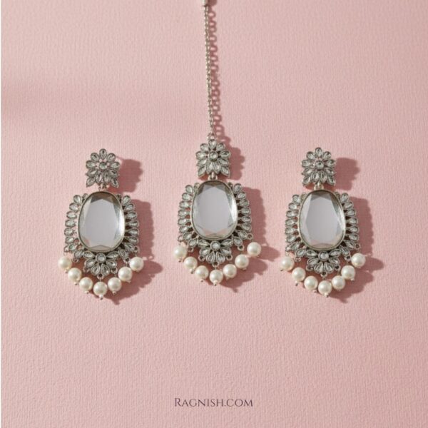 Close-up of Mirror Glaze Kundan chandelier earrings with pearl drops on textured beige background.